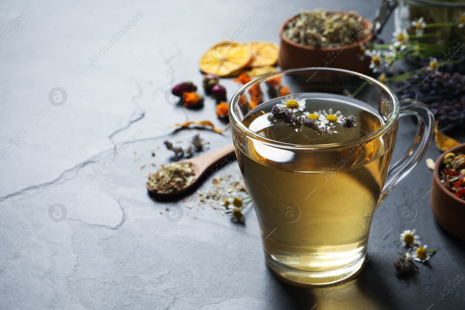 Photo of Glass cup of aromatic freshly brewed tea near different dry herbs on table. Space for text