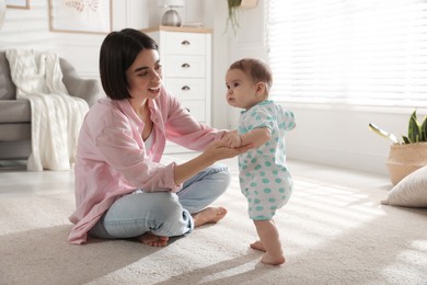 Photo of Mother supporting her baby daughter while she learning to walk at home