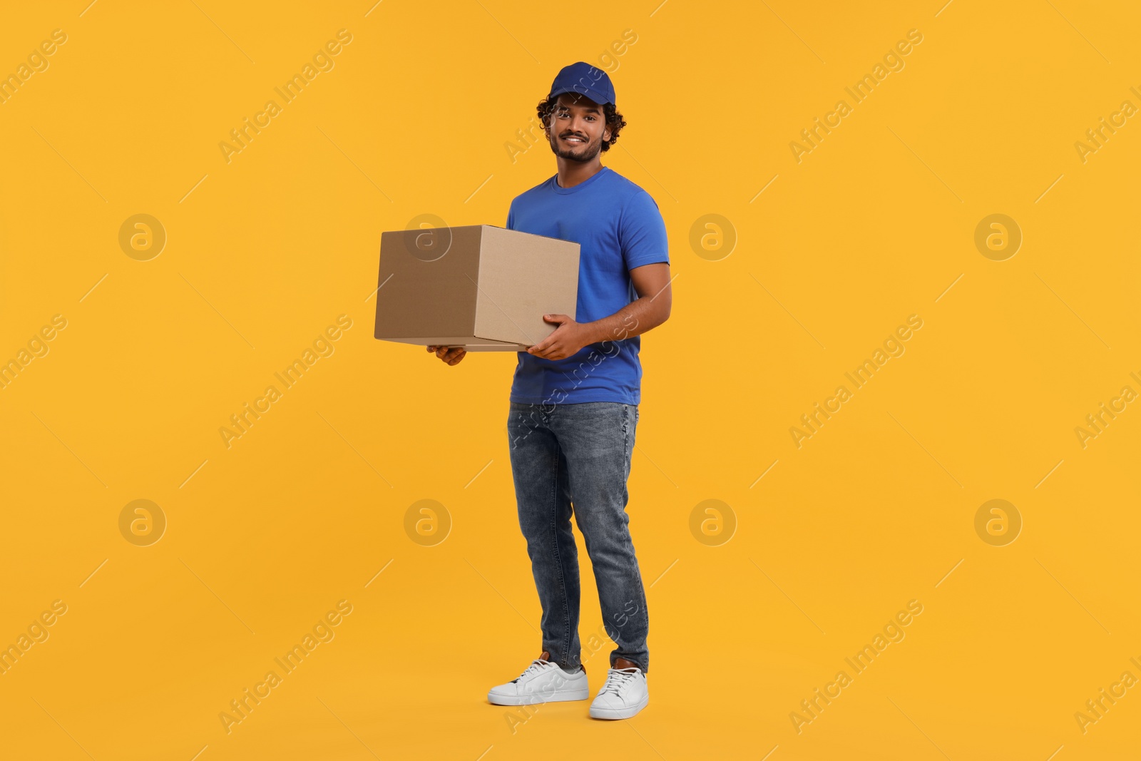 Photo of Happy young courier with parcel on orange background