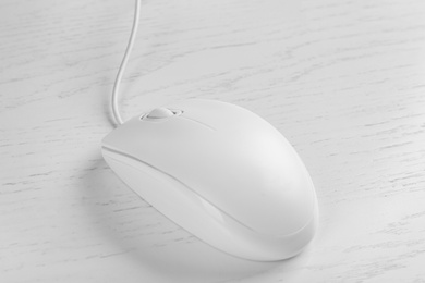 Photo of Modern wired optical mouse on white wooden table, closeup