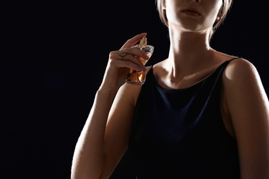 Young woman using perfume on black background, closeup. Space for text