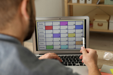 Young man using calendar app on laptop in office, closeup