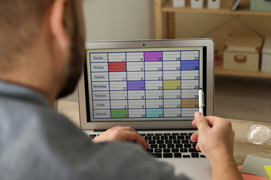 Photo of Young man using calendar app on laptop in office, closeup