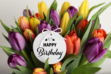 Image of Beautiful bouquet of tulip flowers with Happy Birthday card on light background, closeup