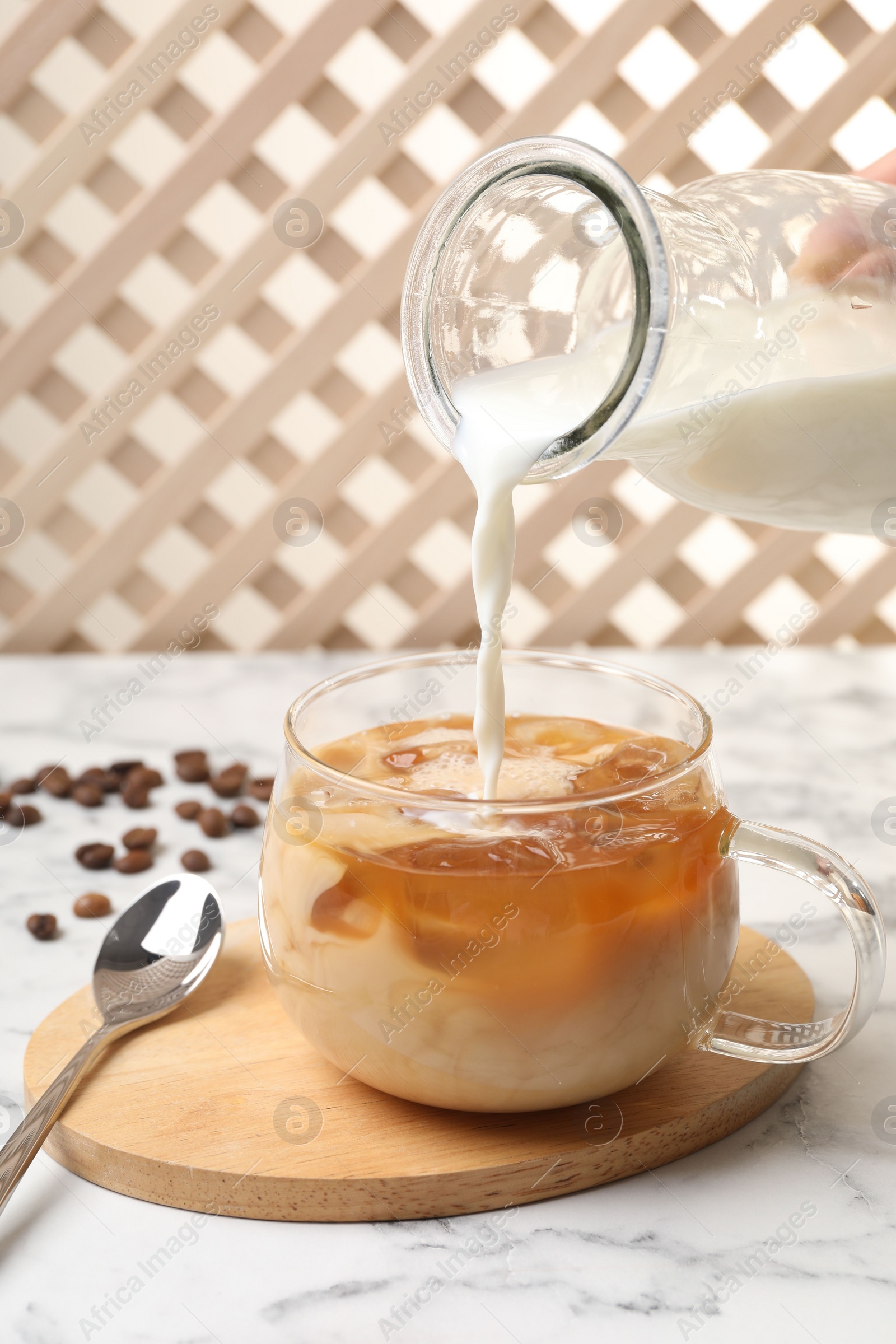 Photo of Woman pouring milk into glass with refreshing iced coffee at white marble table, closeup