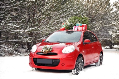 Car with Christmas tree, wreath and gifts in snowy forest on winter day