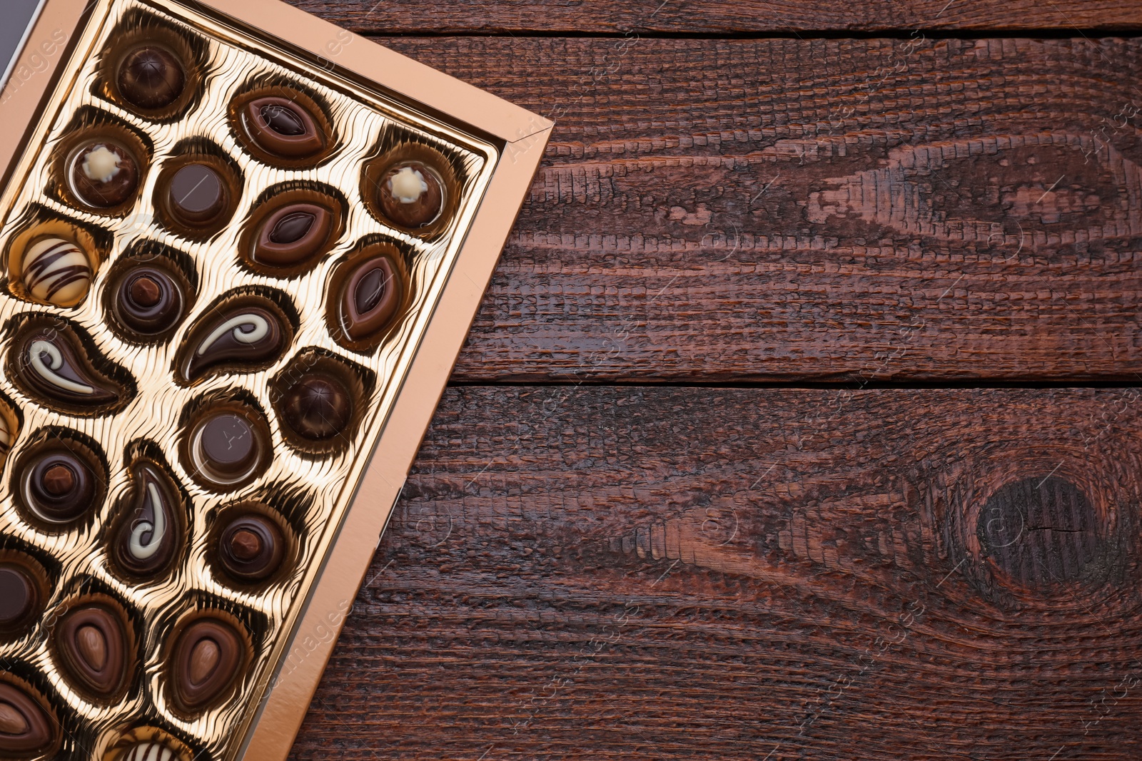 Photo of Box of delicious chocolate candies on wooden table, top view. Space for text