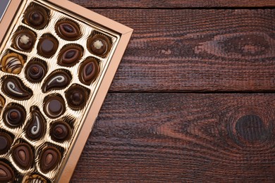 Box of delicious chocolate candies on wooden table, top view. Space for text