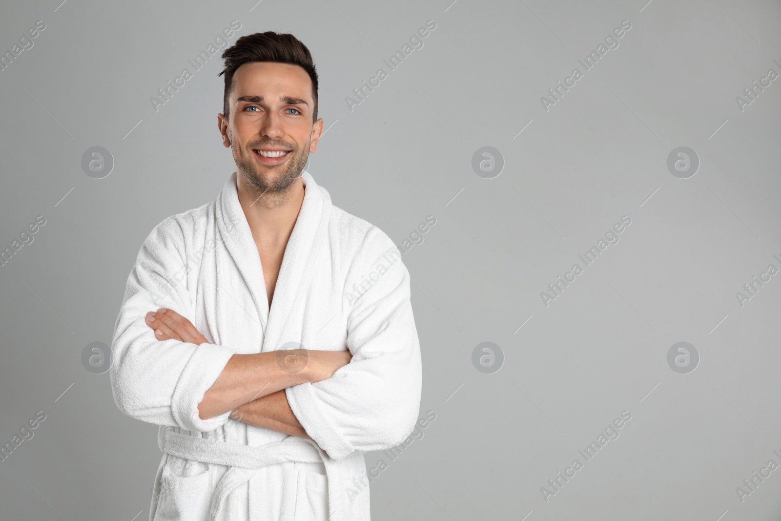 Photo of Happy young man in bathrobe on light grey background. Space for text