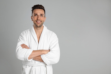 Photo of Happy young man in bathrobe on light grey background. Space for text