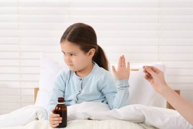 Photo of Daughter refusing to take cough syrup from her mother in bedroom