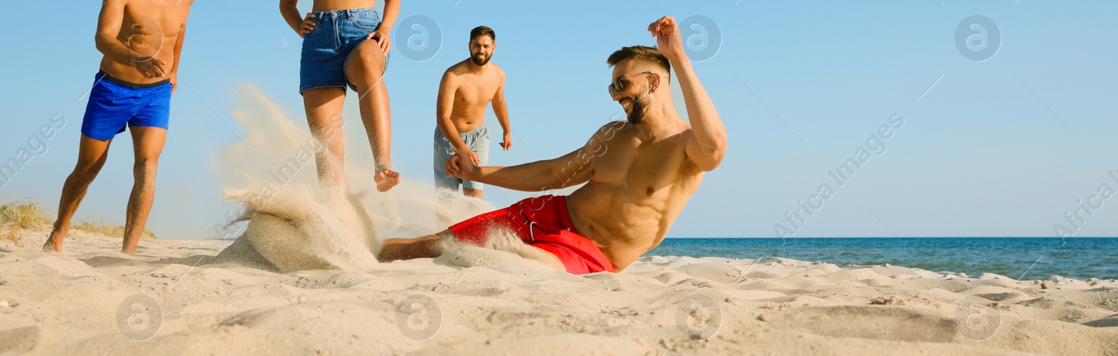 Image of Group of friends playing football on sandy beach, low angle view. Banner design with space for text