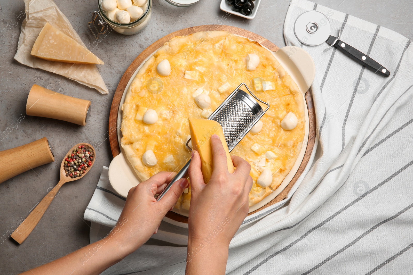 Photo of Woman grating cheese onto homemade pizza on table, top view