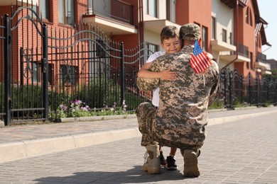 Soldier and his little son with flag of USA hugging outdoors