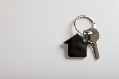 Photo of Key with trinket in shape of house on white background, top view and space for text. Real estate agent services