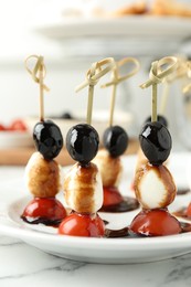 Tasty canapes with black olives, mozzarella and cherry tomatoes on white marble table, closeup