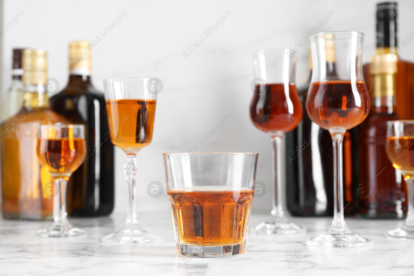 Photo of Delicious liqueurs in glasses and bottles on white marble table