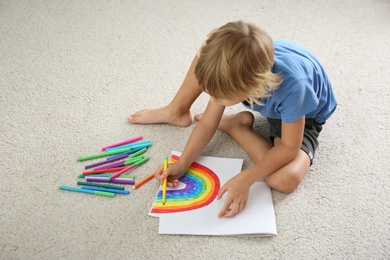 Photo of Little boy drawing rainbow on floor indoors. Stay at home concept