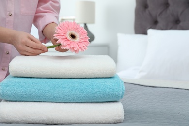 Woman putting flower on stack of clean towels in bedroom. Space for text