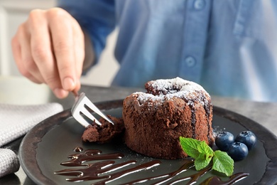 Photo of Woman eating delicious fresh fondant with hot chocolate at table. Lava cake recipe