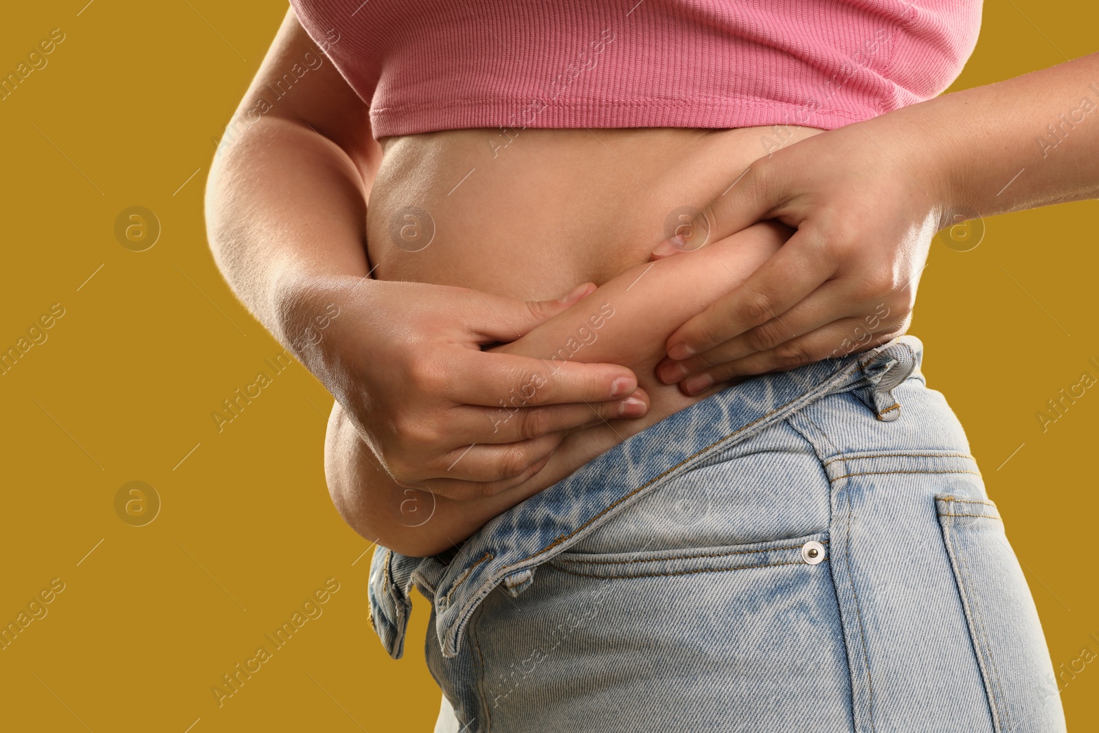 Photo of Woman touching belly fat on goldenrod background, closeup. Overweight problem