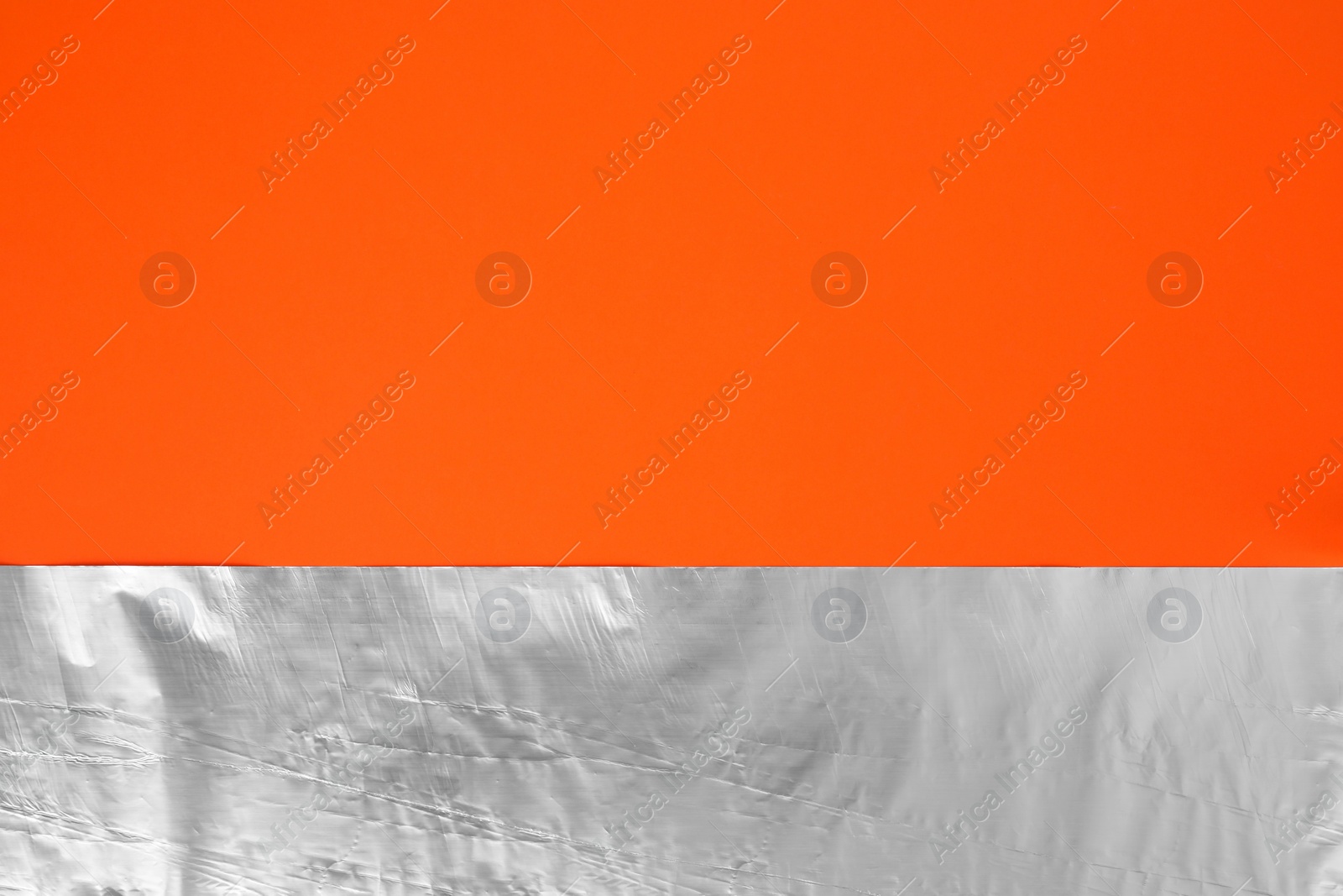 Photo of Sheet of aluminum foil on orange background, top view. Space for text