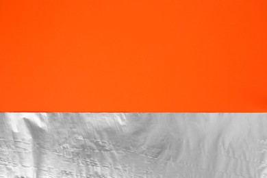 Photo of Sheet of aluminum foil on orange background, top view. Space for text