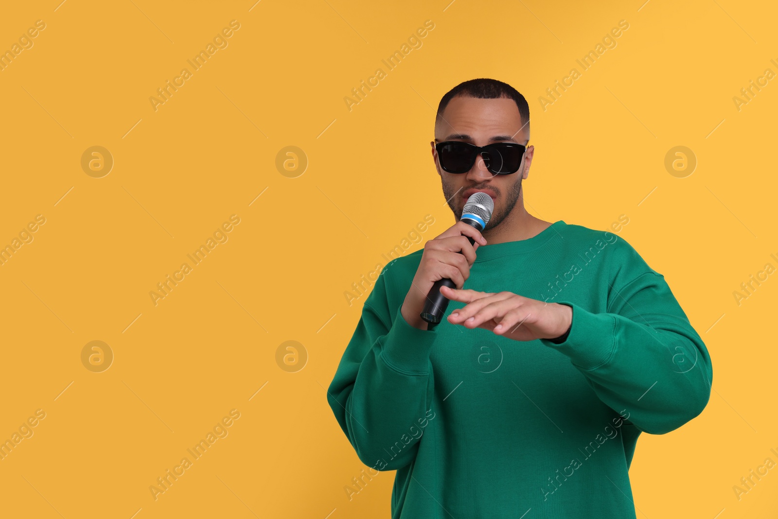 Photo of Handsome man with microphone singing on orange background. Space for text