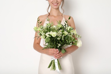 Young bride wearing wedding dress with beautiful bouquet on light background, closeup