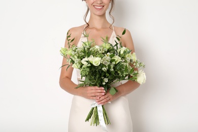 Photo of Young bride wearing wedding dress with beautiful bouquet on light background, closeup