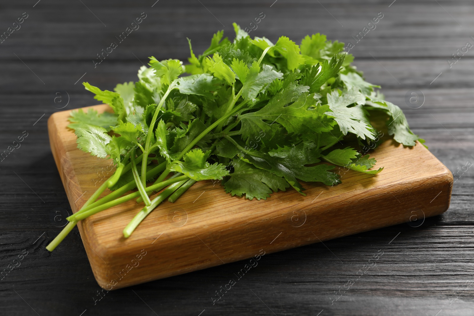 Photo of Fresh green cilantro and board on black wooden table