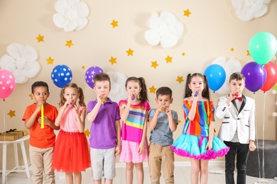 Photo of Adorable children with party blowers indoors. Birthday celebration