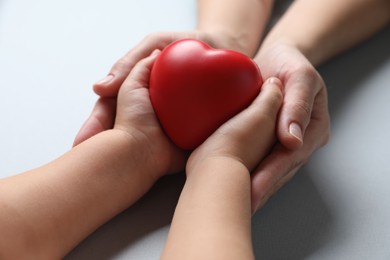 Mother and her child holding red decorative heart on gray background, closeup