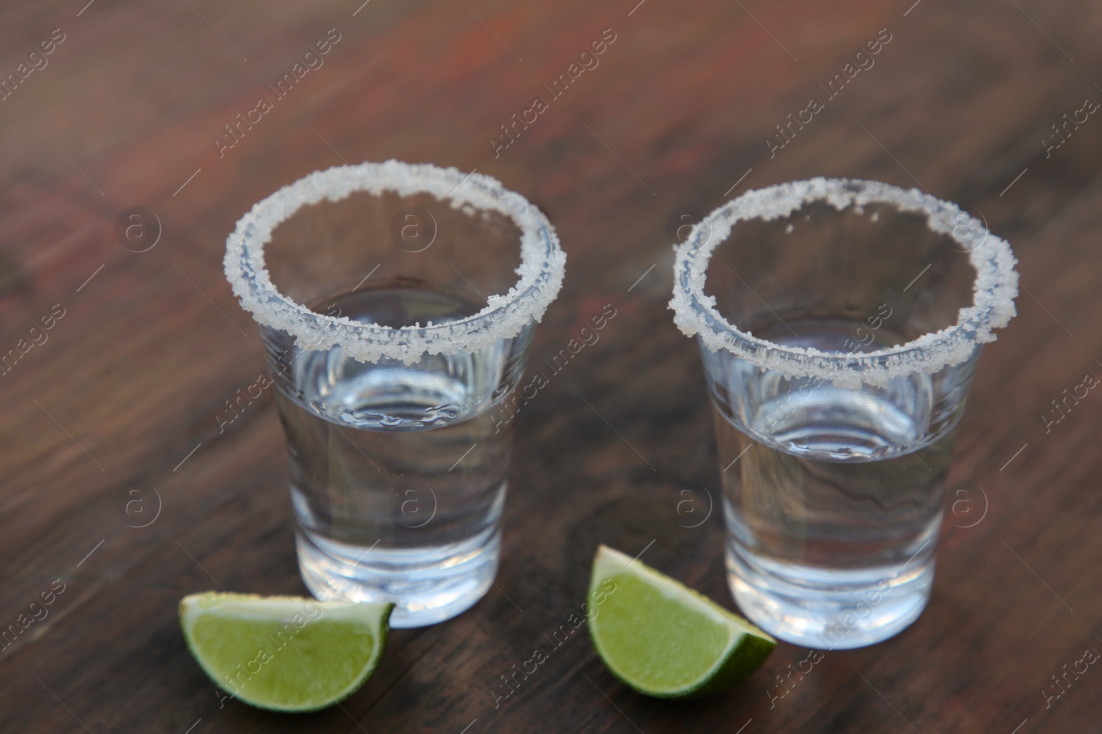 Photo of Mexican tequila shots with lime slices and salt on wooden table, closeup