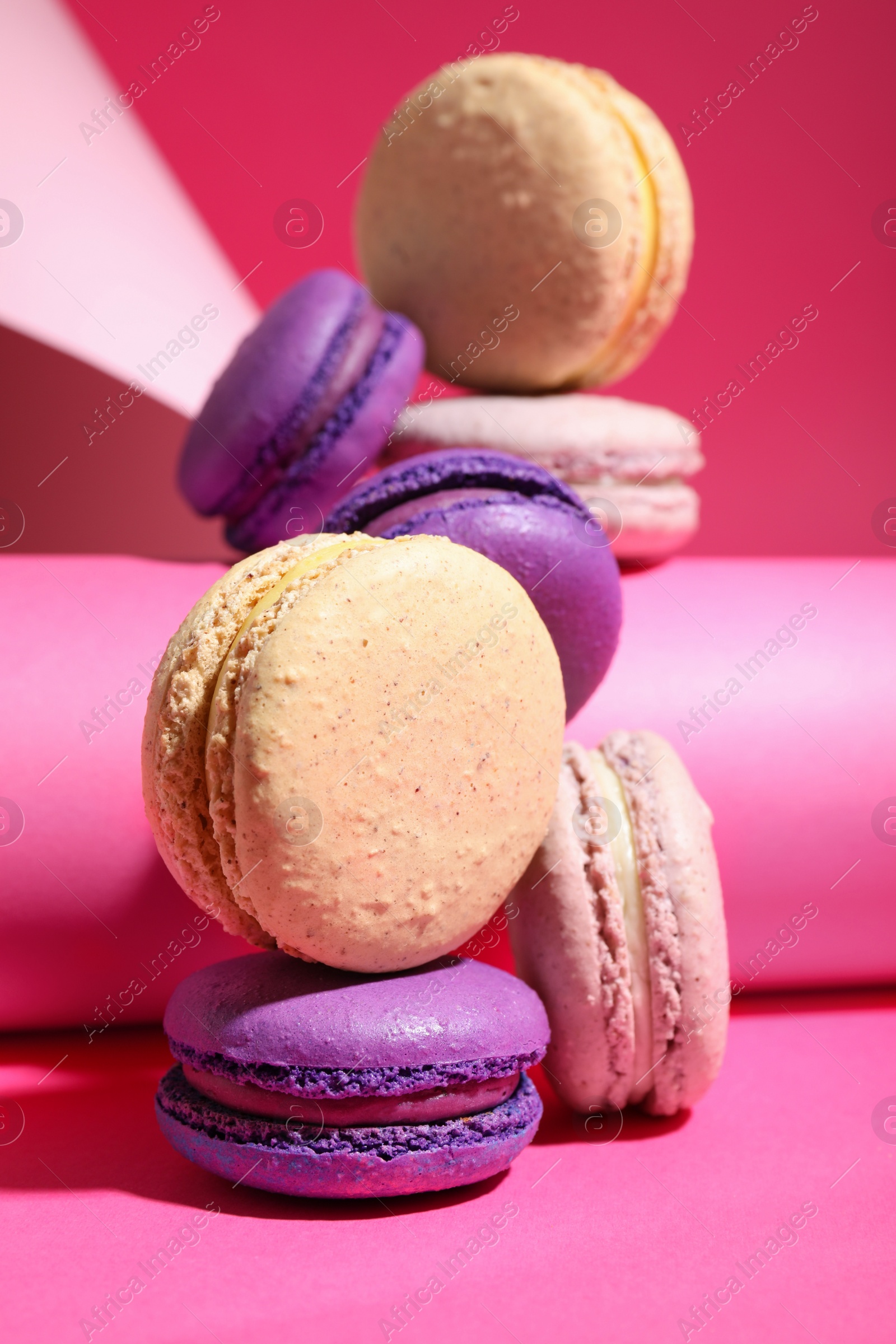 Photo of Delicious fresh colorful macarons and paper roll on pink background