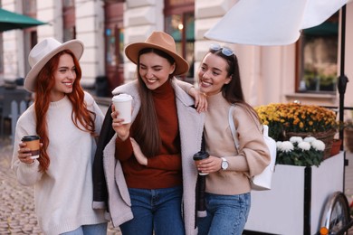 Happy friends with paper cups of coffee spending time together on city street