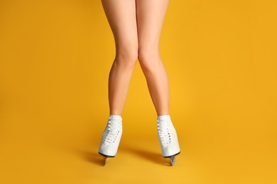 Photo of Woman in elegant white ice skates on yellow background, closeup of legs