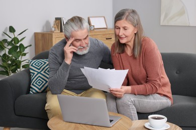 Elderly couple with papers and laptop discussing pension plan in room