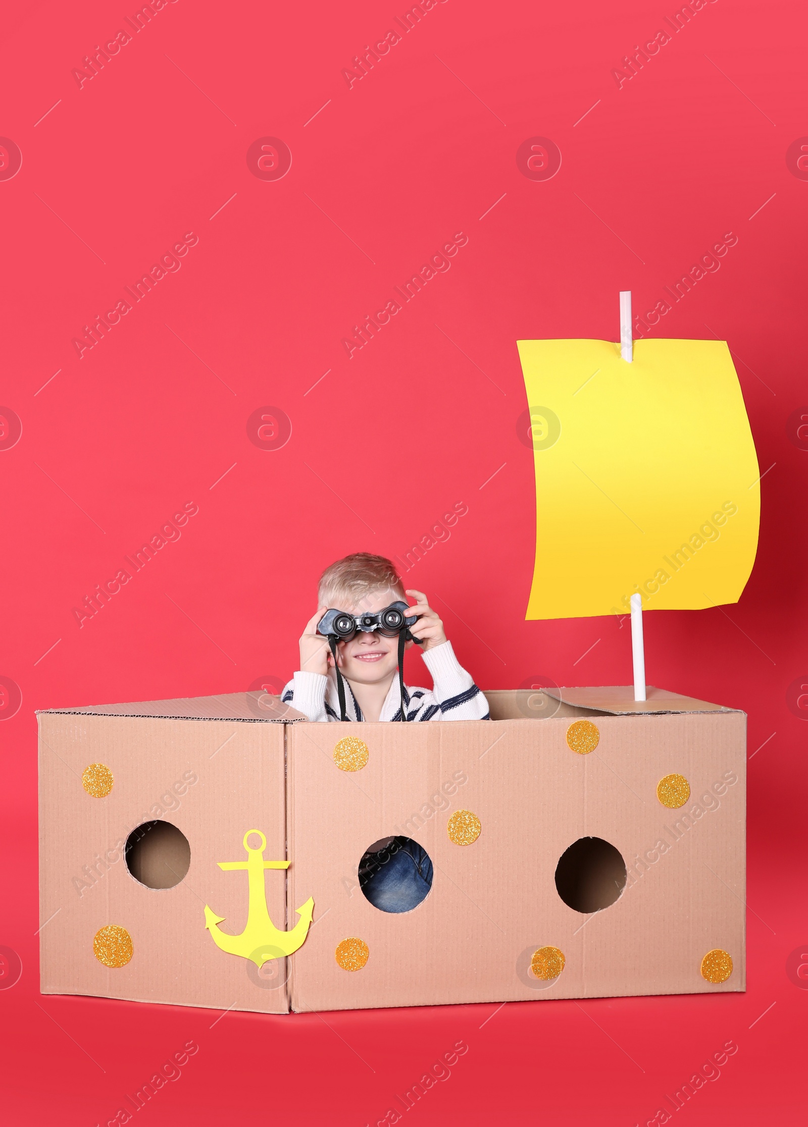 Photo of Little child playing with ship made of cardboard box on red background