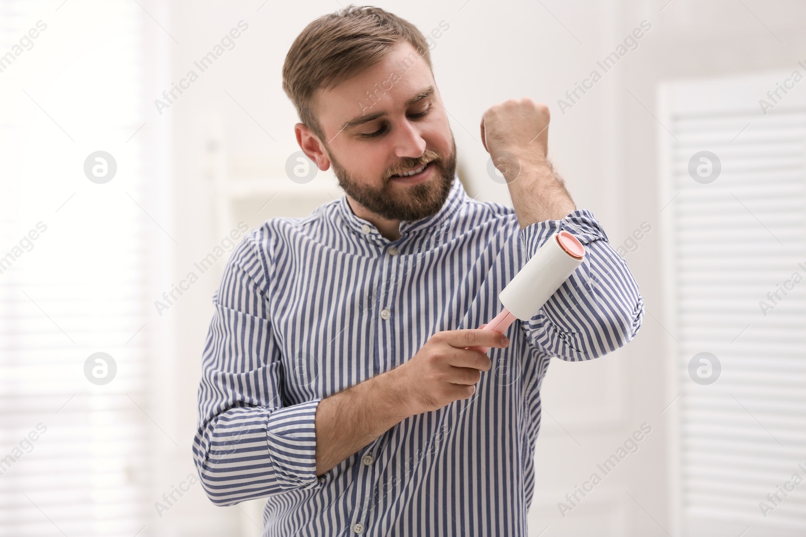 Photo of Young man cleaning clothes with lint roller at home