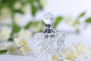 Photo of Aromatic perfume in bottle and beautiful jasmine flowers on white background, closeup