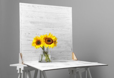 Photo of Glass vase with beautiful sunflowers and double-sided backdrop on table in photo studio