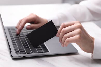 Photo of Woman with laptop holding blank business card at white table, closeup. Space for text