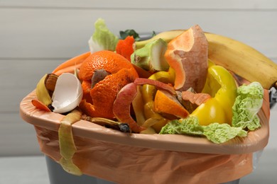 Photo of Trash bin with organic waste for composting on light background, closeup