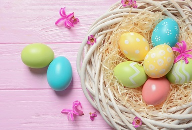 Photo of Flat lay composition of wicker nest with painted Easter eggs on wooden table