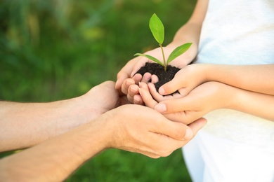 Photo of Family holding soil with green plant in hands on blurred background