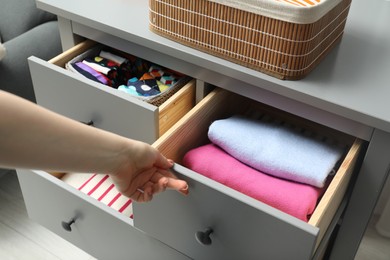 Woman opening drawer with different folded clothes indoors, closeup