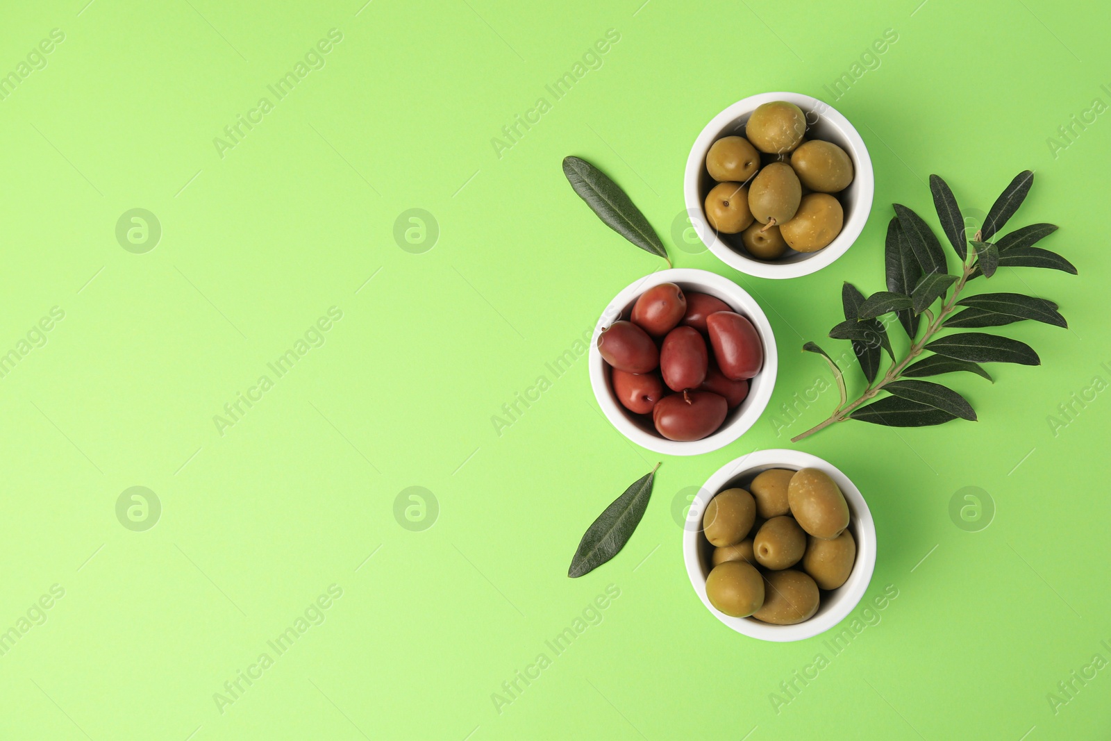 Photo of Different fresh olives and leaves on light green background, flat lay. Space for text