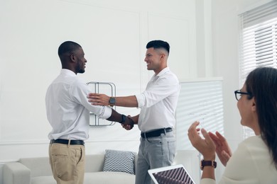 Boss shaking hand with new employee and coworkers applauding in office