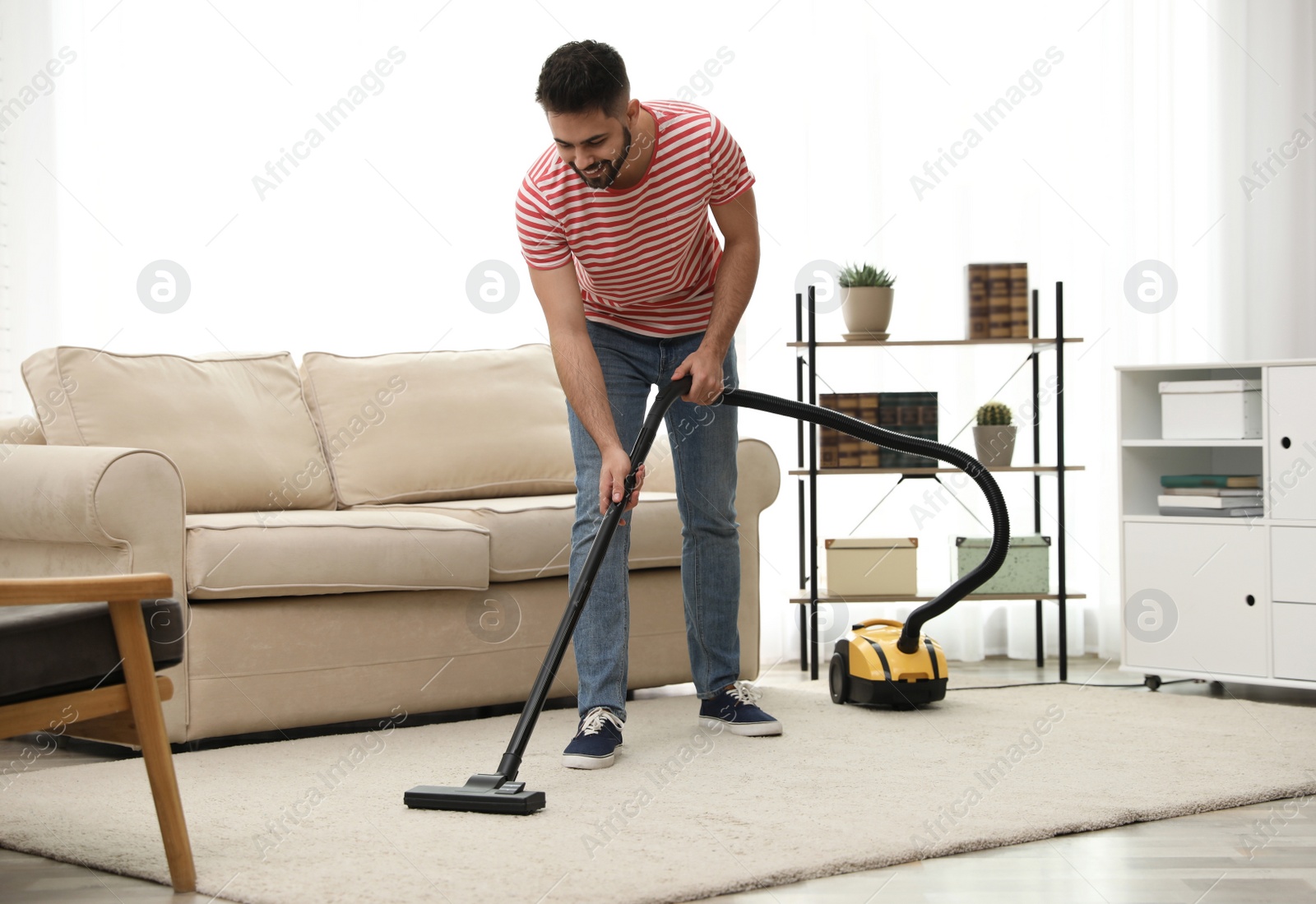 Photo of Young man using vacuum cleaner at home